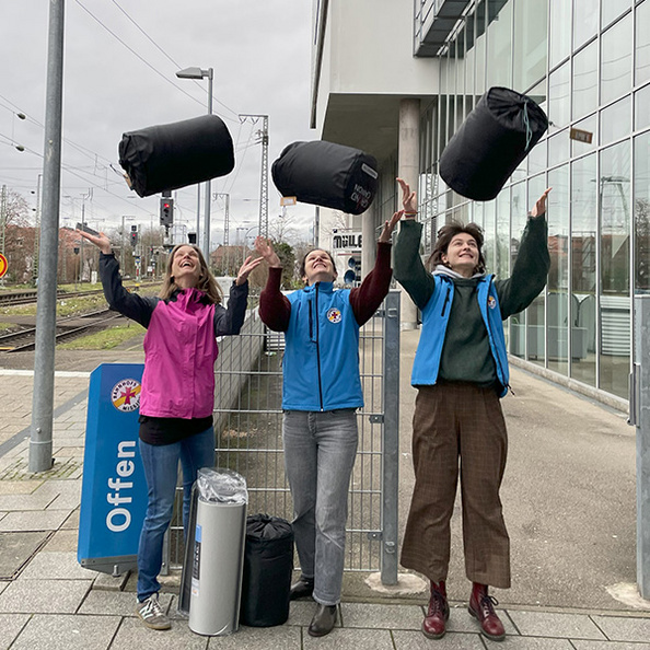 Sarah Gugel (Mitte) und Ellen Graehl (rechts) von der Bahnhofsmission Freiburg werfen gemeinsam mit Tanja Steinbach von Sterr-Kölln & Partner Schlafsäcke in die Luft